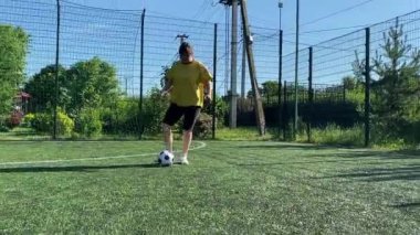 Spor giyimli genç bir kadın sabah futbol sahasında antrenman yapıyor. Spor için adanmışlık ve tutku, sabah egzersizinin özü ve açık havada pratik.