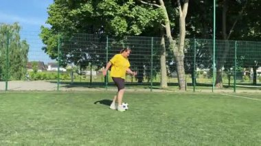 Spor giyimli genç bir kadın sabah futbol sahasında antrenman yapıyor. Spor için adanmışlık ve tutku, sabah egzersizinin özü ve açık havada pratik.