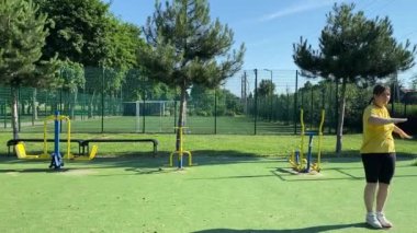 Spor giyim sektöründe genç bir kadın spor yapıyor, spor aletini sabahları spor sahasında fiziksel egzersiz için kullanıyor. Forma olan bağlılığı odaklanma ve enerjiyle eğitim rutinini gerçekleştiriyor.