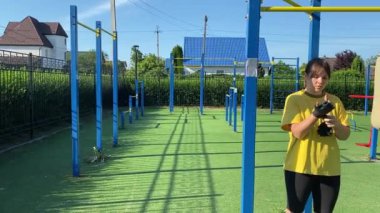 Spor giyim sektöründe genç bir kadın spor yapıyor, spor aletini sabahları spor sahasında fiziksel egzersiz için kullanıyor. Forma olan bağlılığı odaklanma ve enerjiyle eğitim rutinini gerçekleştiriyor.