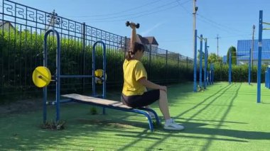 Spor giyim sektöründe genç bir kadın spor yapıyor, spor aletini sabahları spor sahasında fiziksel egzersiz için kullanıyor. Forma olan bağlılığı odaklanma ve enerjiyle eğitim rutinini gerçekleştiriyor.