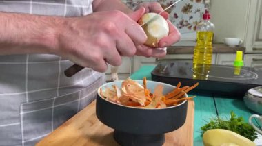 Mutfak konsepti, ev yapımı yemekler için hazırlama malzemeleri. Önlüklü genç bir adam ustalıkla yemek pişiriyor, mutfak tezgahında sebze soyuyor. Ev yemeği ve aşçılık tutkusu