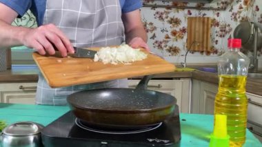 Mutfak konsepti, ev yapımı yemekler için hazırlama malzemeleri. Önlüklü genç bir adam ustalıkla yemek pişiriyor, mutfak tezgahında sebze doğruyor. Ev yemeği ve aşçılık tutkusu