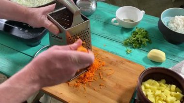 Mutfak konsepti, ev yapımı yemekler için hazırlama malzemeleri. Önlüklü genç bir adam ustaca yemek pişiriyor, mutfak tezgahında havuç rendeliyor. Ev yemeği ve aşçılık tutkusu