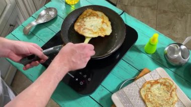 Önlüklü genç bir adam ev mutfağında tavada gözleme pişiriyor. Krepleri ustalıkla çeviriyor ve mükemmel pişirmelerini sağlıyor. Ev yemeği ve aşçılık tutkusu