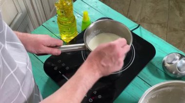 Önlüklü genç bir adam ev mutfağında yemek hazırlıyor, evde krep hazırlıyor. İçindekileri dikkatlice karıştırıyor, yemeği pişirmeye hazırlanıyor. Ev yemeği ve aşçılık becerileri.