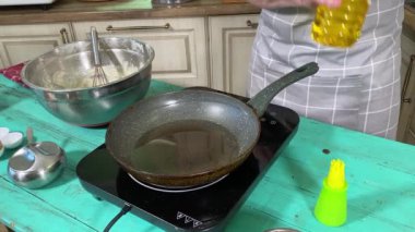 Önlüklü genç bir adam ev mutfağında tavada gözleme pişiriyor. Beyaz bir erkek, mutfak aletine sebze yağı döküyor. Hazırlık süreci. Ev yemeği ve aşçılık tutkusu