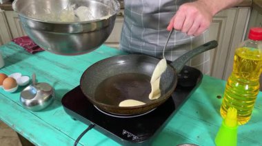 Önlüklü genç bir adam ev mutfağında tavada gözleme pişiriyor. Beyaz bir erkek becerikli bir şekilde çatal bıçakla yemeği şekillendirir. Ev yemeği ve aşçılık tutkusu