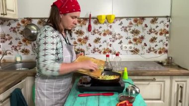 Mutfak konsepti, ev yapımı yemekler için hazırlama malzemeleri. Önlüklü genç bir kadın yemek pişiriyor, mutfak tezgahında sebze soteliyor. Ev yemeği ve gastronomi tutkusu.