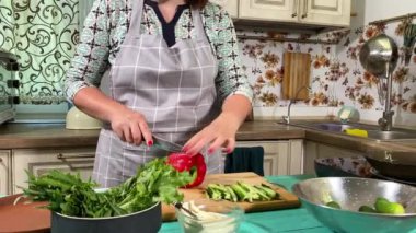 Mutfak konsepti, ev yapımı yemekler için hazırlama malzemeleri. Önlüklü genç bir kadın yemek pişiriyor, mutfak tezgahında sebze kesiyor. Ev yemeği ve gastronomi tutkusu.