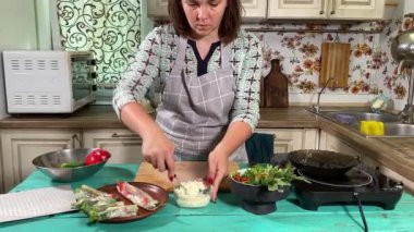 Mutfak konsepti, ev yapımı yemekler için hazırlama malzemeleri. Önlüklü genç bir kadın yemek pişiriyor, mutfak tezgahında sebzeli börek yapıyor. Ev yemeği ve gastronomi.