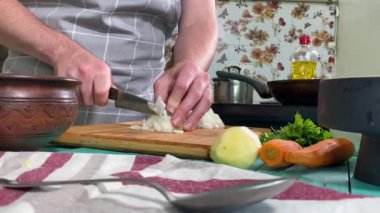 Mutfak konsepti, ev yapımı yemekler için hazırlama malzemeleri. Önlüklü genç bir adam ustalıkla yemek pişiriyor, mutfak tezgahında sebze doğruyor. Ev yemeği ve aşçılık tutkusu