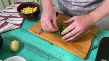 Mutfak konsepti, ev yapımı yemekler için hazırlama malzemeleri. Önlüklü genç bir adam ustalıkla yemek pişiriyor, mutfak tezgahında sebze doğruyor. Ev yemeği ve aşçılık tutkusu