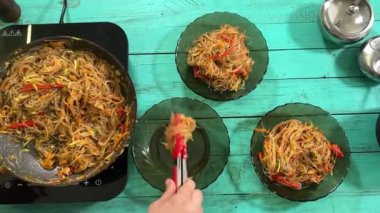 Mutfak konsepti, ev yapımı yemekler için hazırlama malzemeleri. Önlüklü genç bir kadın yemek pişiriyor. Mutfak tezgahında Tayland eriştesi yapıyor. Ev yemeği ve gastronomi tutkusu.