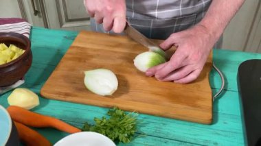 Mutfak konsepti, ev yapımı yemekler için hazırlama malzemeleri. Önlüklü genç bir adam ustalıkla yemek pişiriyor, mutfak tezgahında sebze doğruyor. Ev yemeği ve aşçılık tutkusu