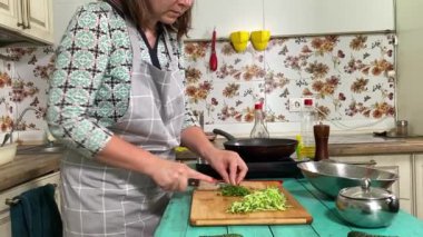 Mutfak konsepti, ev yapımı yemekler için hazırlama malzemeleri. Önlüklü genç bir kadın yemek pişiriyor, mutfak tezgahında sebze kesiyor. Ev yemeği ve gastronomi tutkusu.