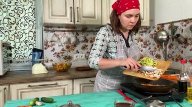 Mutfak konsepti, ev yapımı yemekler için hazırlama malzemeleri. Önlüklü genç bir kadın yemek pişiriyor, mutfak tezgahında sebze soteliyor. Ev yemeği ve gastronomi tutkusu.