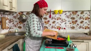 Mutfak konsepti, ev yapımı yemekler için hazırlama malzemeleri. Önlüklü genç bir kadın yemek pişiriyor, mutfak tezgahında sebze soteliyor. Ev yemeği ve gastronomi tutkusu.