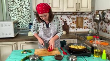 Mutfak konsepti, ev yapımı yemekler için hazırlama malzemeleri. Önlüklü genç bir kadın yemek pişiriyor, mutfak tezgahında sebze kesiyor. Ev yemeği ve gastronomi tutkusu.