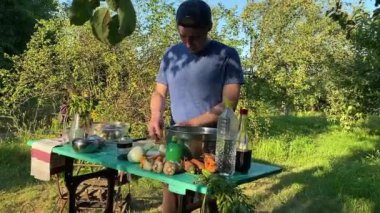 Yakışıklı bir beyaz adam açık hava barbeküsü için malzeme hazırlıyor. Açık ateşte leziz bir yemek. Bahçede yemek pişirmenin rahatlatıcı atmosferine sahip olmanın keyfi. BBQ konsepti