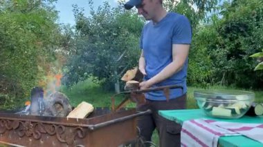 Yakışıklı bir beyaz adam açık hava barbeküsü için malzeme hazırlıyor. Açık ateşte leziz bir yemek. Bahçede yemek pişirmenin rahatlatıcı atmosferine sahip olmanın keyfi. BBQ konsepti