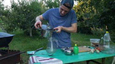 Yakışıklı bir beyaz adam açık havada yemek pişirmek için malzeme hazırlıyor. Açık alanda leziz bir limonata. Arka bahçedeki rahatlama atmosferinin keyfi. BBQ, piknik konsepti