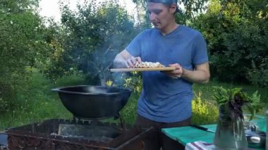 Yakışıklı beyaz bir adam arka bahçedeki ızgaranın üzerinde kazanda lezzetli bir yemek hazırlıyor. Açık hava yemekleri, barbekü geleneği, arka bahçe eğlencesi, gevşeme konusunda aşçılık becerileri. BBQ konsepti