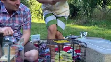 Genç bir baba ve oğul arka bahçede kemirgenlerle ilgilenerek birlikte güzel vakit geçirmenin keyfini çıkarıyorlar. Aile ve çocuk, küçük hayvanlarına sevgi dolu bir şekilde açık hava ortamında bakıyorlar.