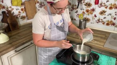 Genç ve çekici bir ev hanımı ev mutfağında hamur mayası hazırlıyor. Kadın malzemeleri karıştırıyor, mükemmel bir temel oluşturmak için hamur üzerinde hassasiyetle çalışıyor. Geleneksel pişirme ve ev yapımı aşçılık becerileri