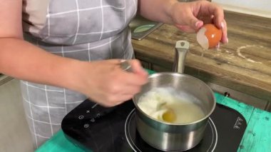 Genç ve çekici bir ev hanımı ev mutfağında hamur mayası hazırlıyor. Kadın malzemeleri karıştırıyor, mükemmel bir temel oluşturmak için hamur üzerinde hassasiyetle çalışıyor. Geleneksel pişirme ve ev yapımı aşçılık becerileri