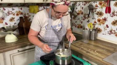 Genç ve çekici bir ev hanımı ev mutfağında hamur mayası hazırlıyor. Kadın malzemeleri karıştırıyor, mükemmel bir temel oluşturmak için hamur üzerinde hassasiyetle çalışıyor. Geleneksel pişirme ve ev yapımı aşçılık becerileri