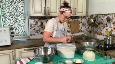 Genç ve çekici bir ev hanımı ev mutfağında hamur mayası hazırlıyor. Kadın malzemeleri karıştırıyor, mükemmel bir temel oluşturmak için hamur üzerinde hassasiyetle çalışıyor. Geleneksel pişirme ve ev yapımı aşçılık becerileri