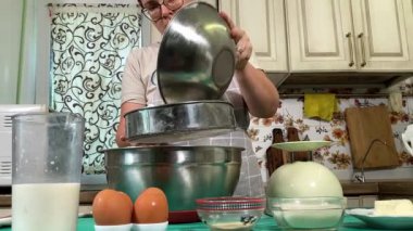 Genç ve çekici bir ev hanımı ev mutfağında hamur mayası hazırlıyor. Kadın malzemeleri karıştırıyor, mükemmel bir temel oluşturmak için hamur üzerinde hassasiyetle çalışıyor. Geleneksel pişirme ve ev yapımı aşçılık becerileri
