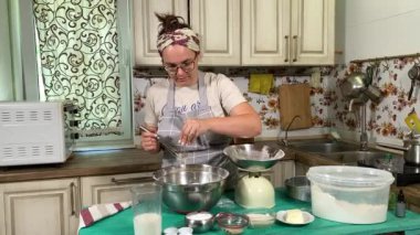 Genç ve çekici bir ev hanımı ev mutfağında hamur mayası hazırlıyor. Kadın malzemeleri karıştırıyor, mükemmel bir temel oluşturmak için hamur üzerinde hassasiyetle çalışıyor. Geleneksel pişirme ve ev yapımı aşçılık becerileri