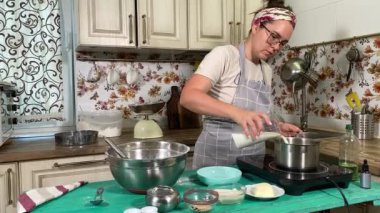 Genç ve çekici bir ev hanımı ev mutfağında hamur mayası hazırlıyor. Kadın malzemeleri karıştırıyor, mükemmel bir temel oluşturmak için hamur üzerinde hassasiyetle çalışıyor. Geleneksel pişirme ve ev yapımı aşçılık becerileri