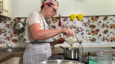 Genç ve çekici bir ev hanımı ev mutfağında hamur mayası hazırlıyor. Kadın malzemeleri karıştırıyor, mükemmel bir temel oluşturmak için hamur üzerinde hassasiyetle çalışıyor. Geleneksel pişirme ve ev yapımı aşçılık becerileri