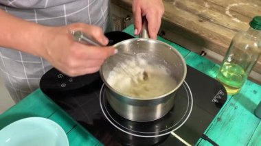 Genç ve çekici bir ev hanımı ev mutfağında hamur mayası hazırlıyor. Kadın malzemeleri karıştırıyor, mükemmel bir temel oluşturmak için hamur üzerinde hassasiyetle çalışıyor. Geleneksel pişirme ve ev yapımı aşçılık becerileri