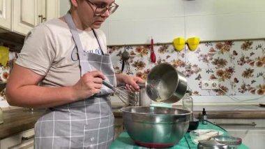 Genç ve çekici bir ev hanımı ev mutfağında hamur mayası hazırlıyor. Kadın malzemeleri karıştırıyor, mükemmel bir temel oluşturmak için hamur üzerinde hassasiyetle çalışıyor. Geleneksel pişirme ve ev yapımı aşçılık becerileri