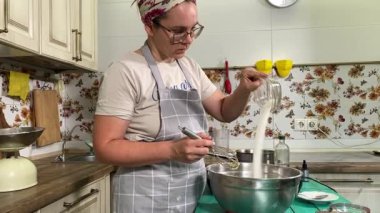 Genç ve çekici bir ev hanımı ev mutfağında hamur mayası hazırlıyor. Kadın malzemeleri karıştırıyor, mükemmel bir temel oluşturmak için hamur üzerinde hassasiyetle çalışıyor. Geleneksel pişirme ve ev yapımı aşçılık becerileri