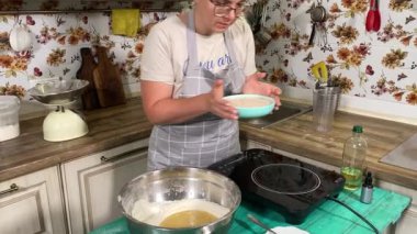 Genç ve çekici bir ev hanımı ev mutfağında hamur mayası hazırlıyor. Kadın malzemeleri karıştırıyor, mükemmel bir temel oluşturmak için hamur üzerinde hassasiyetle çalışıyor. Geleneksel pişirme ve ev yapımı aşçılık becerileri