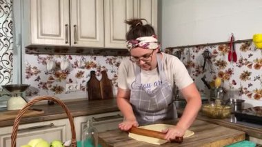 Genç ve çekici bir ev hanımı sıcak mutfağında ev yapımı elmalı turta hazırlıyor. Çekici kadın hamur mayası ve elma dolgusu ile geleneksel pişirme yöntemlerini vurgulayarak ustalıkla çalışıyor.