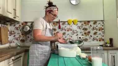 Genç ve çekici bir ev hanımı ev mutfağında hamur mayası hazırlıyor. Kadın malzemeleri karıştırıyor, mükemmel bir temel oluşturmak için hamur üzerinde hassasiyetle çalışıyor. Geleneksel pişirme ve ev yapımı aşçılık becerileri