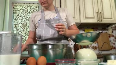 Genç ve çekici bir ev hanımı ev mutfağında hamur mayası hazırlıyor. Kadın malzemeleri karıştırıyor, mükemmel bir temel oluşturmak için hamur üzerinde hassasiyetle çalışıyor. Geleneksel pişirme ve ev yapımı aşçılık becerileri