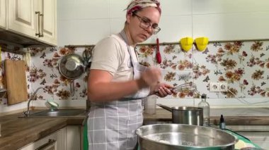 Genç ve çekici bir ev hanımı ev mutfağında hamur mayası hazırlıyor. Kadın malzemeleri karıştırıyor, mükemmel bir temel oluşturmak için hamur üzerinde hassasiyetle çalışıyor. Geleneksel pişirme ve ev yapımı aşçılık becerileri