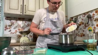 Genç ve çekici bir ev hanımı ev mutfağında hamur mayası hazırlıyor. Kadın malzemeleri karıştırıyor, mükemmel bir temel oluşturmak için hamur üzerinde hassasiyetle çalışıyor. Geleneksel pişirme ve ev yapımı aşçılık becerileri