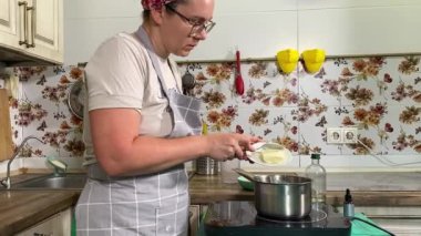 Genç ve çekici bir ev hanımı ev mutfağında hamur mayası hazırlıyor. Kadın malzemeleri karıştırıyor, mükemmel bir temel oluşturmak için hamur üzerinde hassasiyetle çalışıyor. Geleneksel pişirme ve ev yapımı aşçılık becerileri