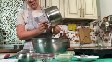 Genç ve çekici bir ev hanımı ev mutfağında hamur mayası hazırlıyor. Kadın malzemeleri karıştırıyor, mükemmel bir temel oluşturmak için hamur üzerinde hassasiyetle çalışıyor. Geleneksel pişirme ve ev yapımı aşçılık becerileri