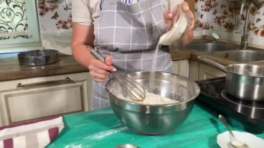 Genç ve çekici bir ev hanımı ev mutfağında hamur mayası hazırlıyor. Kadın malzemeleri karıştırıyor, mükemmel bir temel oluşturmak için hamur üzerinde hassasiyetle çalışıyor. Geleneksel pişirme ve ev yapımı aşçılık becerileri