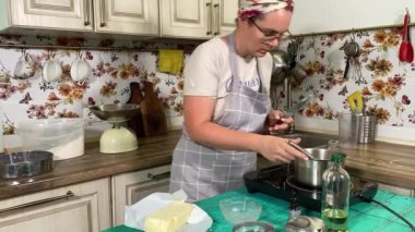 Genç ve çekici bir ev hanımı ev mutfağında hamur mayası hazırlıyor. Kadın malzemeleri karıştırıyor, mükemmel bir temel oluşturmak için hamur üzerinde hassasiyetle çalışıyor. Geleneksel pişirme ve ev yapımı aşçılık becerileri