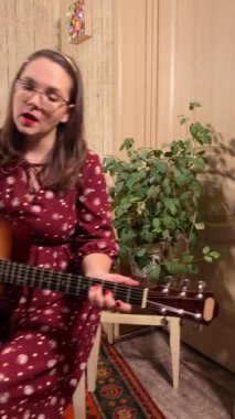 Şık elbiseli ve gözlüklü güzel bir genç kadın evde çalışırken gitar çalar. İçeride yaratıcılığın ve adanmışlığın huzurlu bir anı. Hobi ve boş zaman